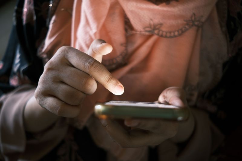 A hand reaching toward a phone screen, the finger about to tap